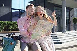 Young happy loving couple looking at map and sitting on scooter