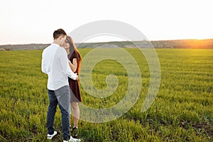 Young, happy, loving couple, at sunset, standing in a green field, against the sky, in the arms, and enjoying each other, advertis