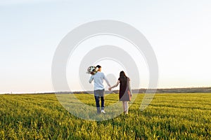 Young, happy, loving couple, at sunset, standing in a green field, against the sky holding hands, and enjoying each other, adverti