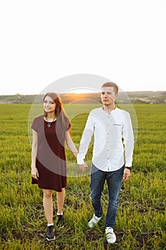 Young, happy, loving couple, at sunset, standing in a green field, against the sky holding hands, and enjoying each other, adverti