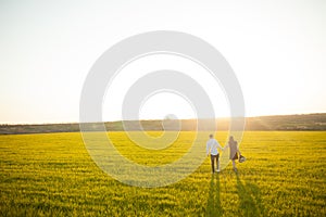 Young, happy, loving couple, at sunset, standing in a green field, against the sky holding hands, and enjoying each other, adverti