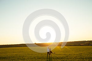 Young, happy, loving couple, at sunset, standing in a green field, against the sky holding hands, and enjoying each other, adverti