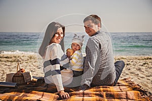 Young happy loving family with small child, enjoying time at beach sitting and hugging near ocean, happy lifestyle family concept