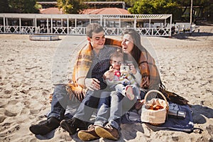 Young happy loving family with small child at picnic, enjoying time at beach sitting and hugging near ocean