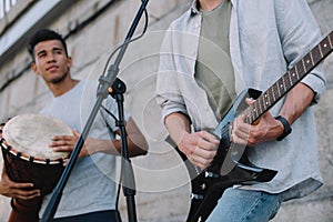 Young happy male buskers playing guitar and djembe