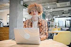 Young happy male freelancer in casual clothes sitting in cafe with laptop and using mobile phone.