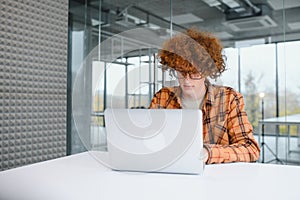 Young happy male freelancer in casual clothes sitting in cafe with laptop and using mobile phone.