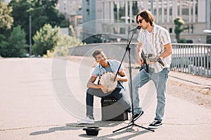 Young and happy male street musicians playing guitar and djembe