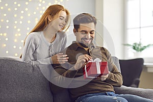 Young happy man boyfriend opening present box from his loving smiling girlfriend