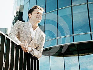 Young happy man in a business suit poses near a modern business center on a summer day