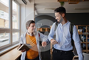 Young happy man with Down syndrome with his mentoring friend celebrating success indoors at school.