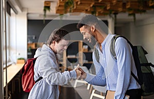 Young happy man with Down syndrome with his mentoring friend greeting indoors at school.