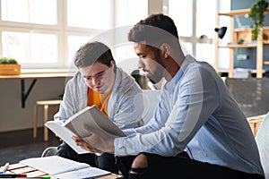 Young happy man with Down syndrome and his tutor studying indoors at school.