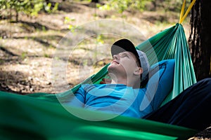 Young happy man in hat relaxing outside in hammock in forest.