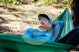 Young happy man in hat relaxing outside in hammock in forest.