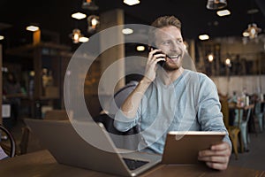 Young happy man having phone call in cafe