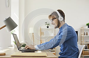Young happy man in headphones typing on laptop and using internet web online services.