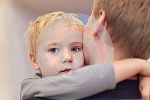 Young happy man holding his cute son. Baby boy embraces the male neck. Serious little kid with blue eyes napping in parent arms. S