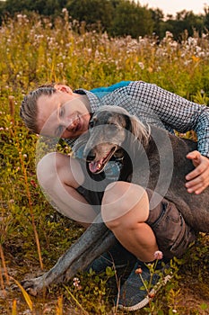Young happy man hugs a dog outdoors. The owner spends time with his pet