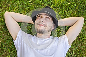 Young happy man is lying and relaxing in grass in park and thinking or dreaming