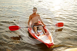 Young Happy Man Paddling Kayak on Beautiful River or Lake at Sunset