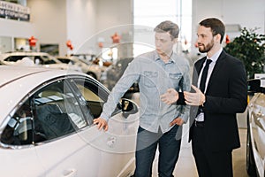 Young happy man preparing to buy new car in auto dealership.