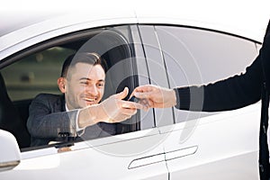 Young Happy Man Receiving Car Keys to Her New Automobile. Dealer giving key to new owner in auto show or salon. Car