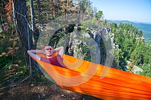 Young happy man relaxing lying in hammock on top of mountain. Summer travel lifestyle.