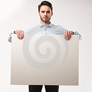 Young happy man showing presentation, pointing on placard over gray background