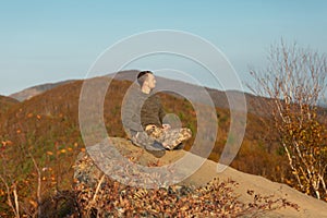 Young and happy man sitting at the top of the mountain. Landscape view of misty autumn mountain hills and man silhouette