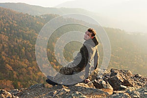 Young and happy man sitting at the top of the mountain. Landscape view of misty autumn mountain hills and man silhouette