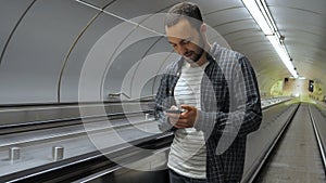 Young happy man surfing internet on his phone while standing on escalator.