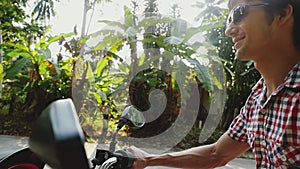 Young happy man traveler in sunglasses driving motorbike on tropical sunny road. slow motion. lens flare effects