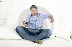 Young happy man watching tv sitting at home living room sofa looking relaxed enjoying television