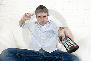 Young happy man watching tv sitting at home living room sofa looking relaxed enjoying television