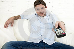 Young happy man watching tv sitting at home living room sofa looking relaxed enjoying television