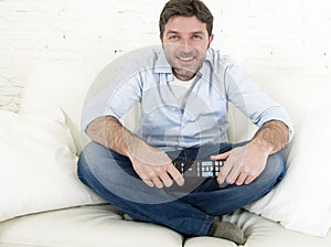 Young happy man watching tv sitting at home living room sofa looking relaxed enjoying television