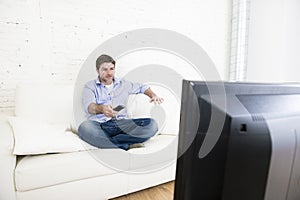 Young happy man watching tv sitting at home living room sofa looking relaxed enjoying television