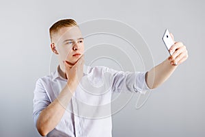 Young happy man in white shirt makes selfie with smartphone