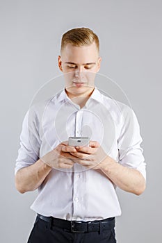 Young happy man in white shirt stands with smartphone