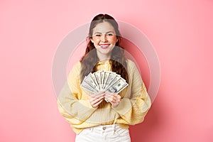 Young happy millennial girl showing dollar bills, holding money with pleased face, winning cash prize, going shopping