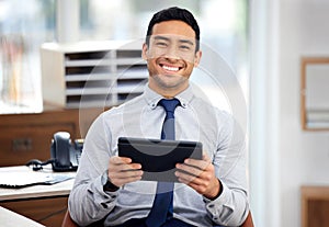 Young happy mixed race businessman holding and using a digital tablet sitting in an office at work. Content hispanic