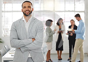 Young happy mixed race businessman standing with his arms crossed while in an office with colleagues. Hispanic male boss