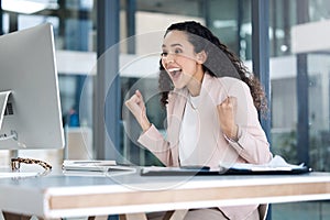 Young happy mixed race businesswoman cheering with joy using a desktop computer in an office. One cheerful hispanic