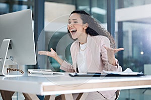 Young happy mixed race businesswoman looking shocked and amazed using a desktop computer in an office. One cheerful