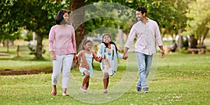 Young happy mixed race family holding hands and walking together in a park. Loving parents spending time with their