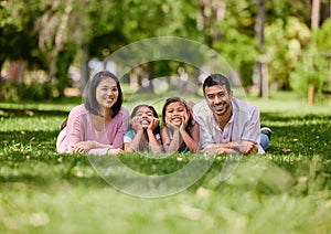 Young happy mixed race family relaxing and lying on grass together in a park. Loving parents spending time with their