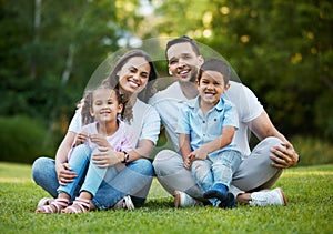 Young happy mixed race family relaxing and sitting on grass in a park together. Loving parents spending time with their