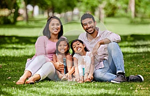 Young happy mixed race family relaxing and sitting on grass together in a park. Loving hispanic parents spending time