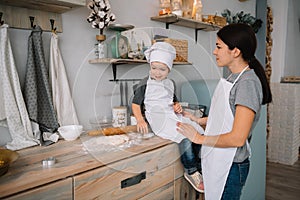 Young happy mom and her baby cook cookies at home in the kitchen. Christmas Homemade Gingerbread. cute boy with mother in white